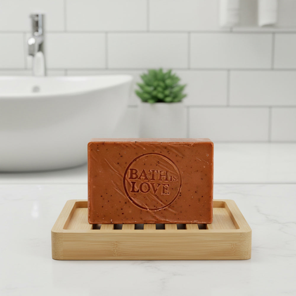 Bar of soap with 'Bath is Love' text on a wooden soap dish in a bathroom setting.