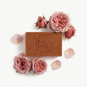 Bar of soap with 'Bath is Love' branding surrounded by pink roses on a white background
