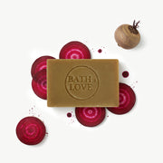 Bar of soap with 'Bath is Love' branding surrounded by sliced beets on a white background