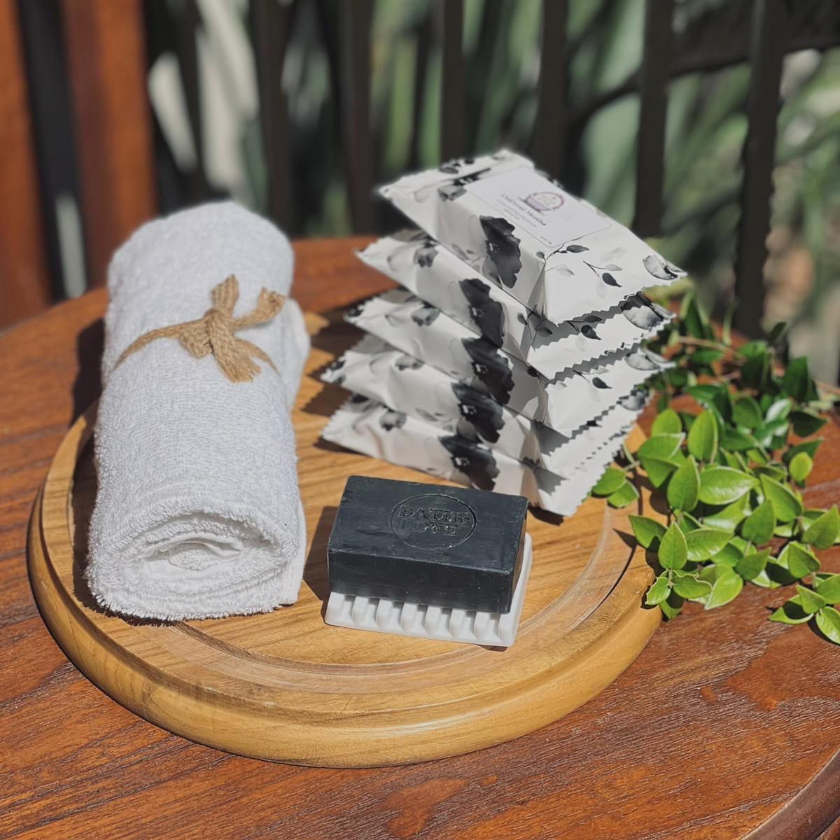 Set of soap bars, a towel, and a scrubber on a wooden tray with a natural background.