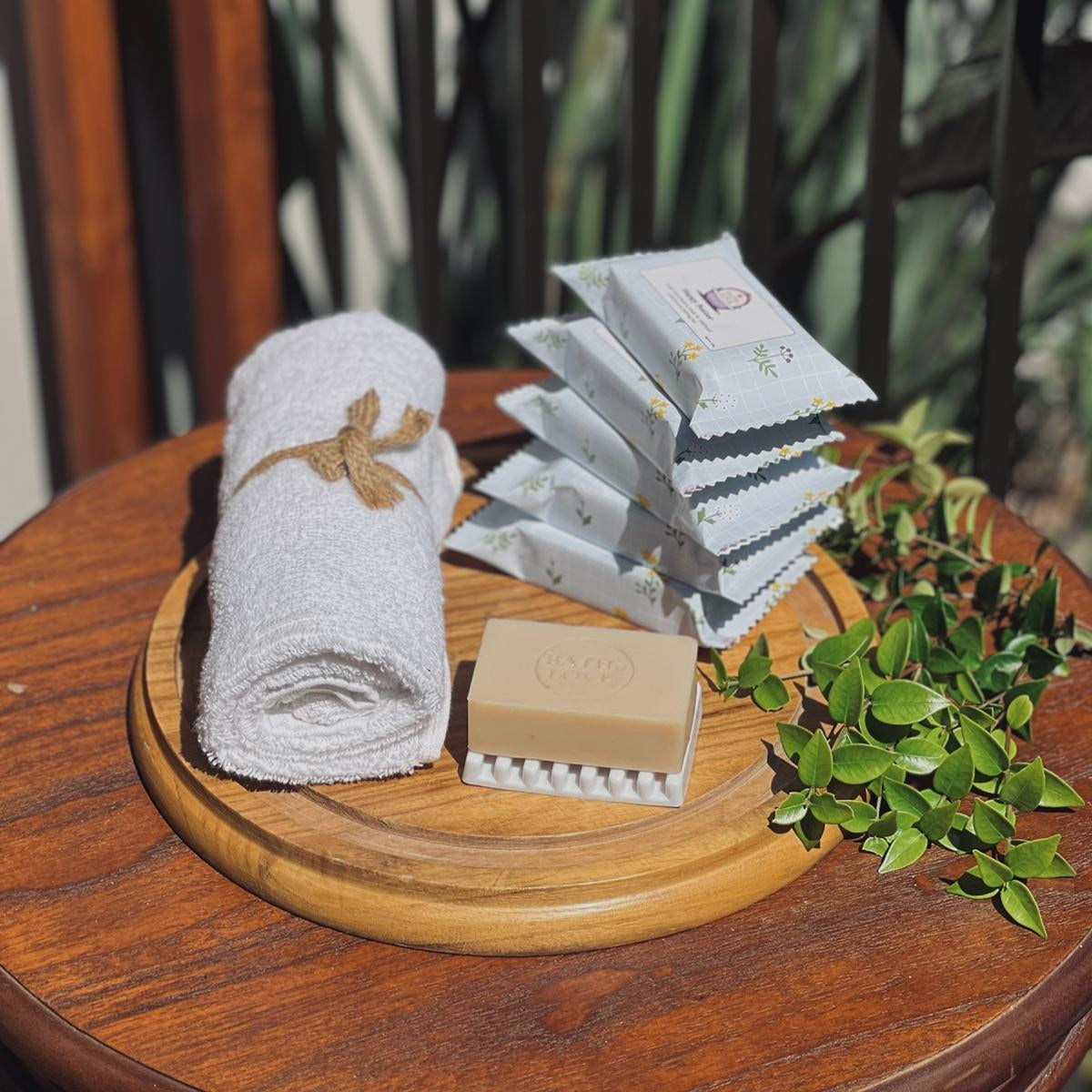 Wooden tray with rolled towel, soap, and tea bags on a wooden surface with blurred natural background